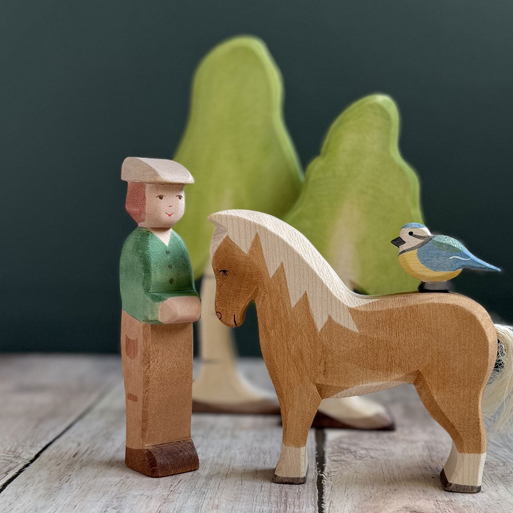 A wooden figure scene with a young boy, a brown horse, and a blue and yellow bird with wooden trees in the background