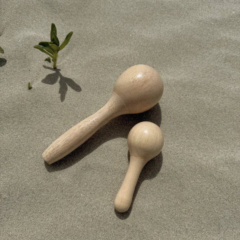 One large and one small wooden maraca on sandy ground with a small plant in the background