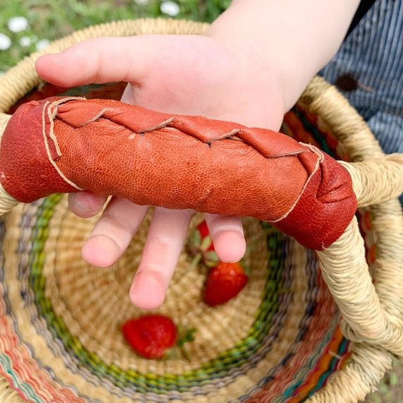 Hand holding a red leather-wrapped handle of a woven basket with strawberries on a natural background