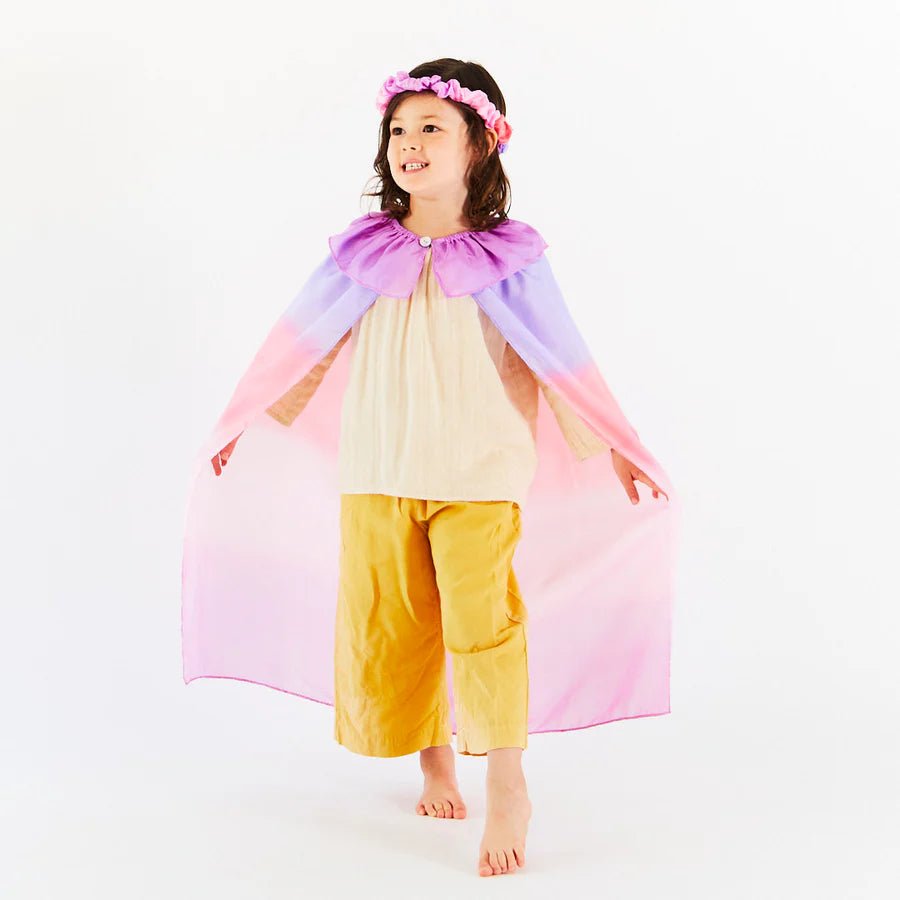 Child wearing a colorful pink and purple cape and yellow pants on a white background