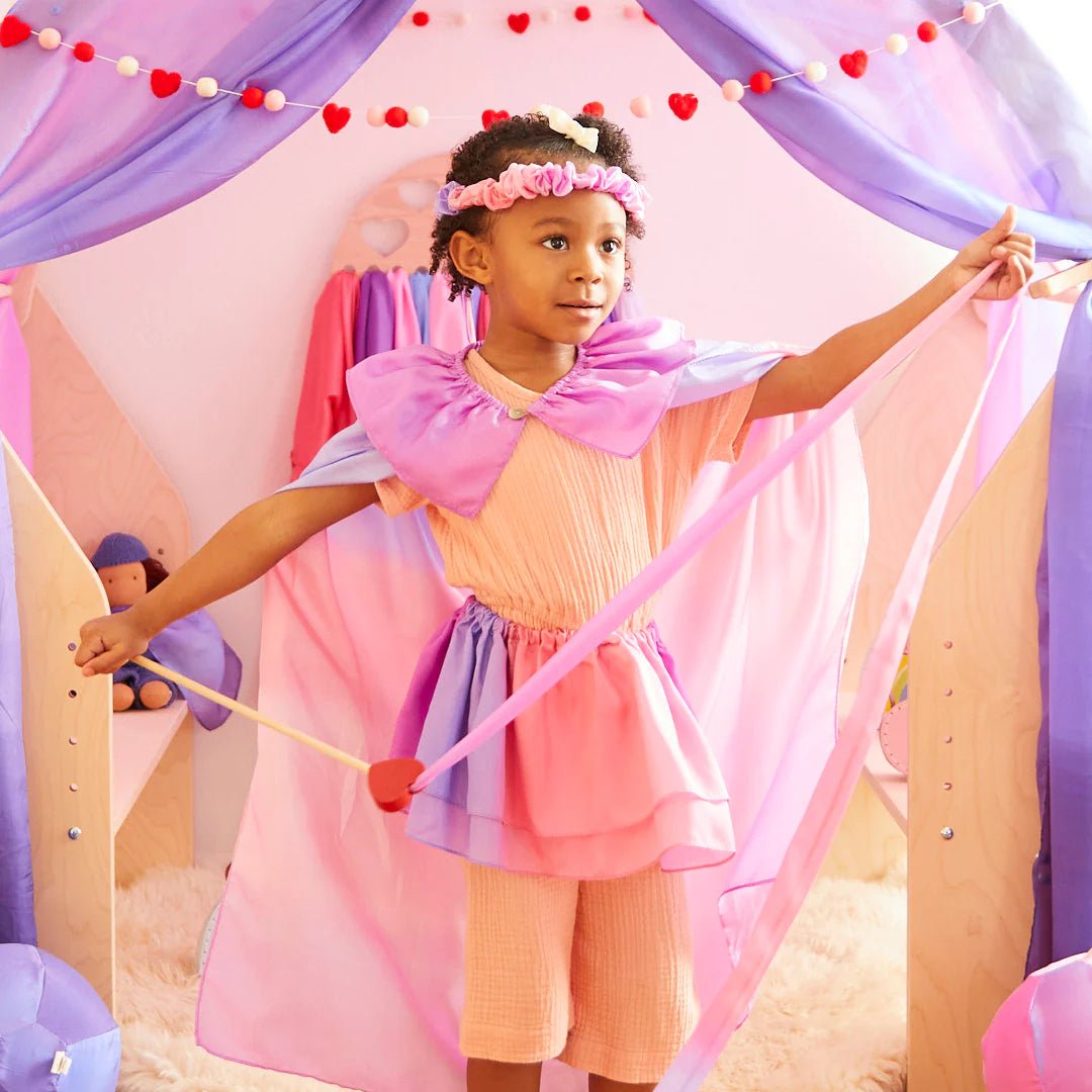 Young girl wearing a pink and purple costume playing inside a play tent.