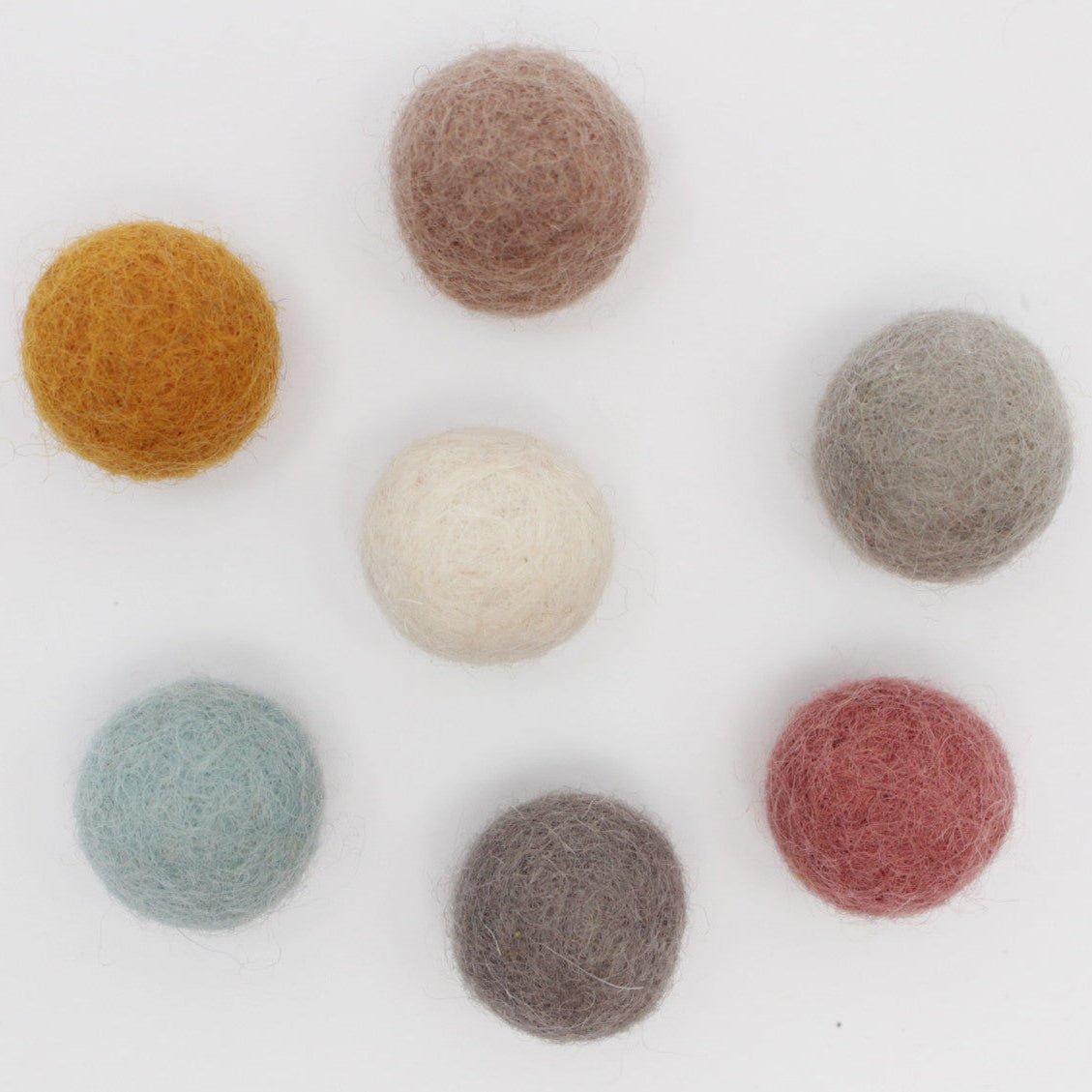 7 felt balls in earth tones on a white background