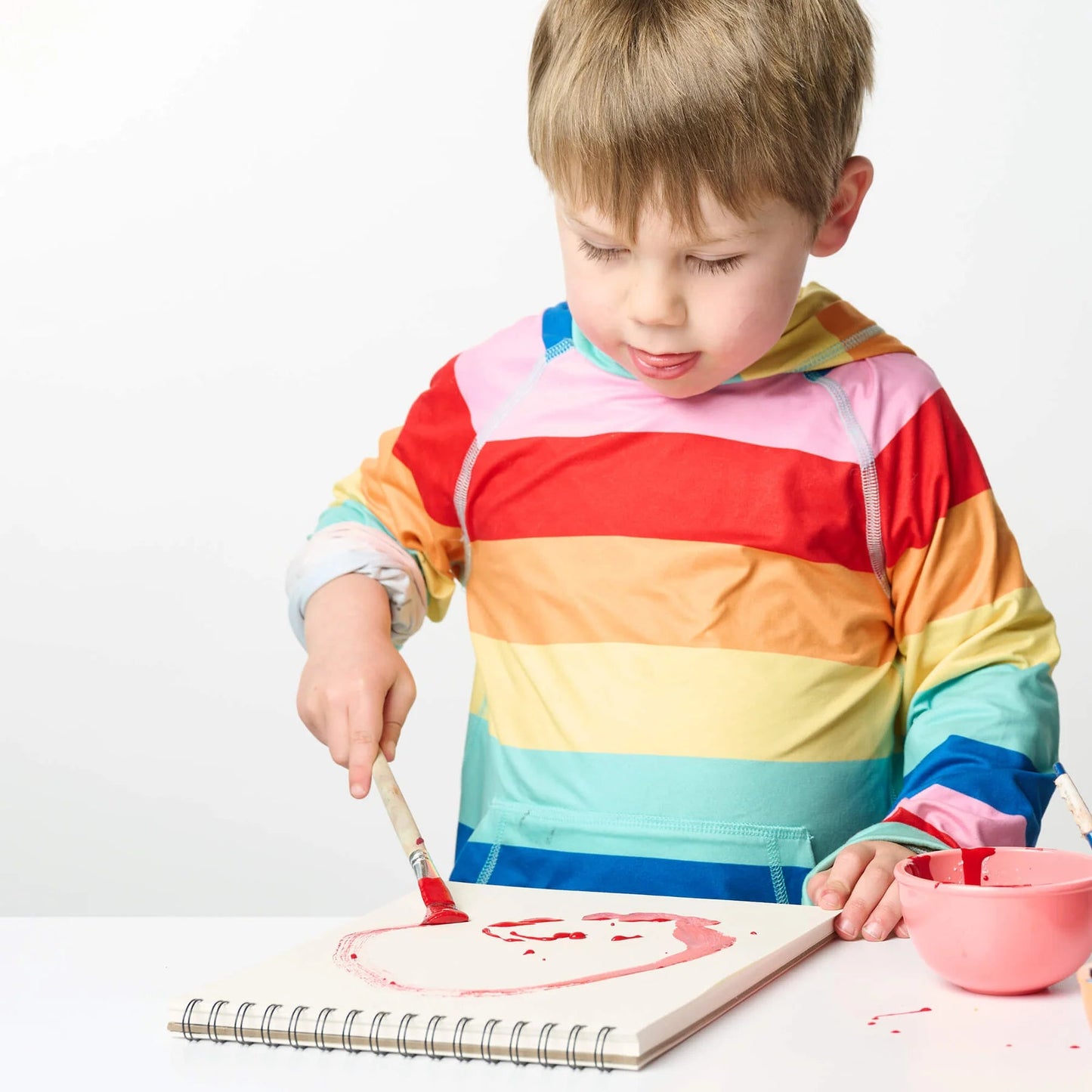 Child in a colorful striped shirt painting on a white surface