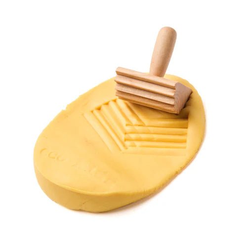 Yellow eco-dough with textured wooden roller on a white background