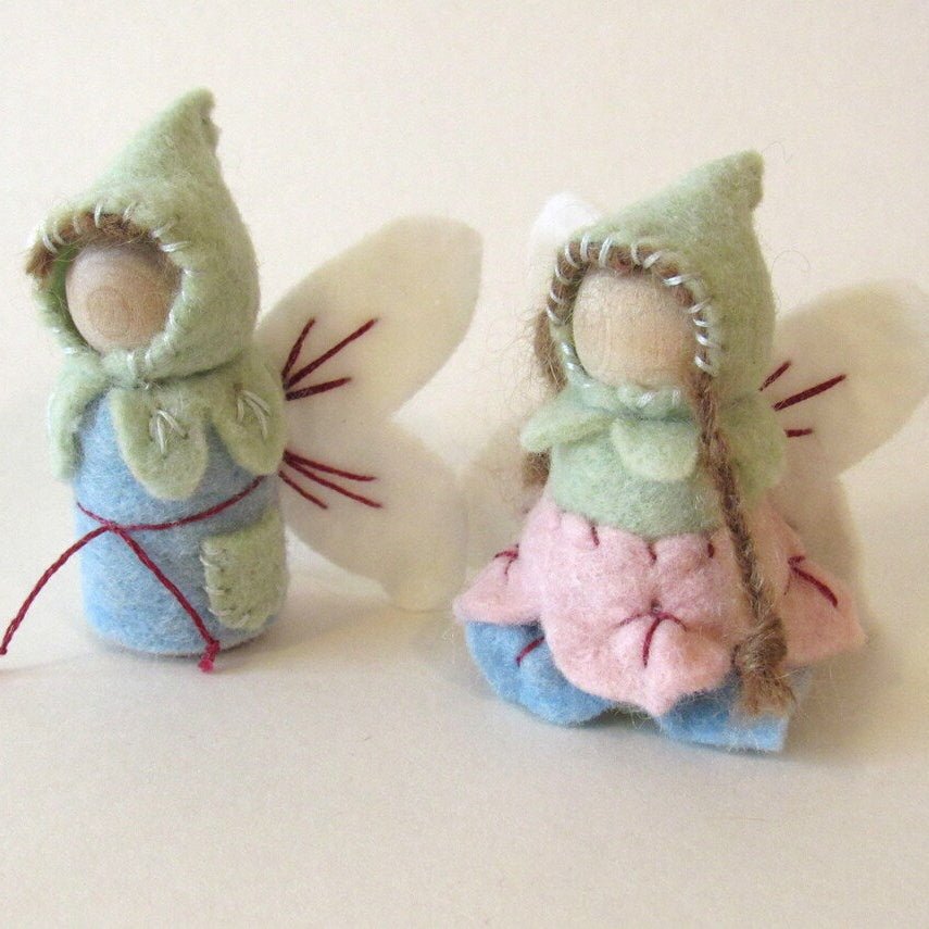 Two small figurines with green hats and colorful dresses on a light background