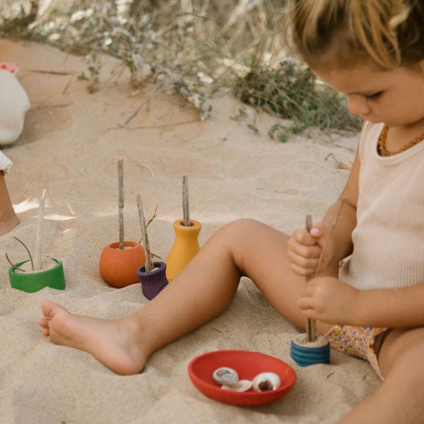 Child playing with colorful wooden pots on a sandy surface
