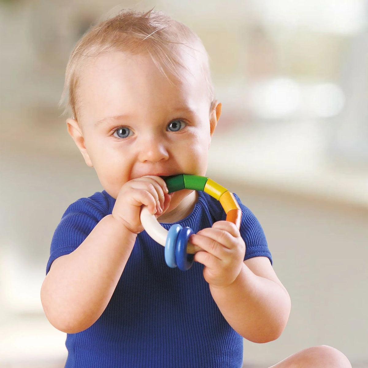 Baby holding a colorful teething ring with a blurred background