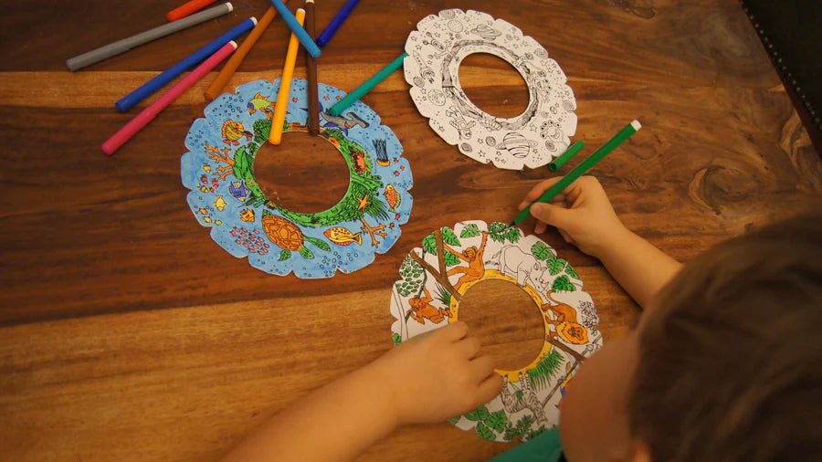 Child coloring in throwing discs with markers on a wooden table.