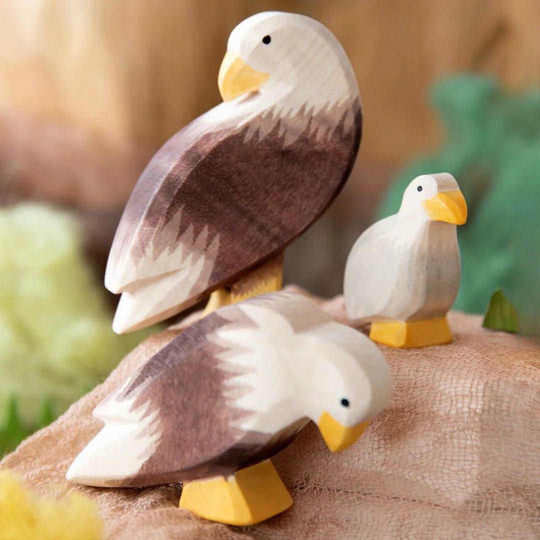 Scene with two wooden eagle figurines and an eaglet perched on a wooden landscape