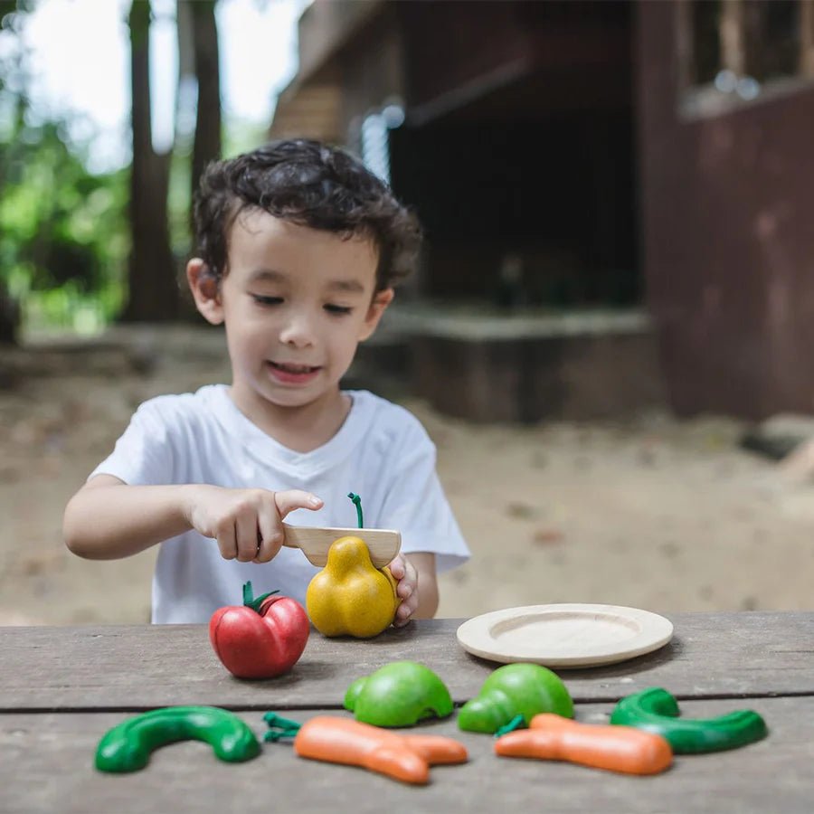 Child playing with toy vegetables on a wooden table outdoors