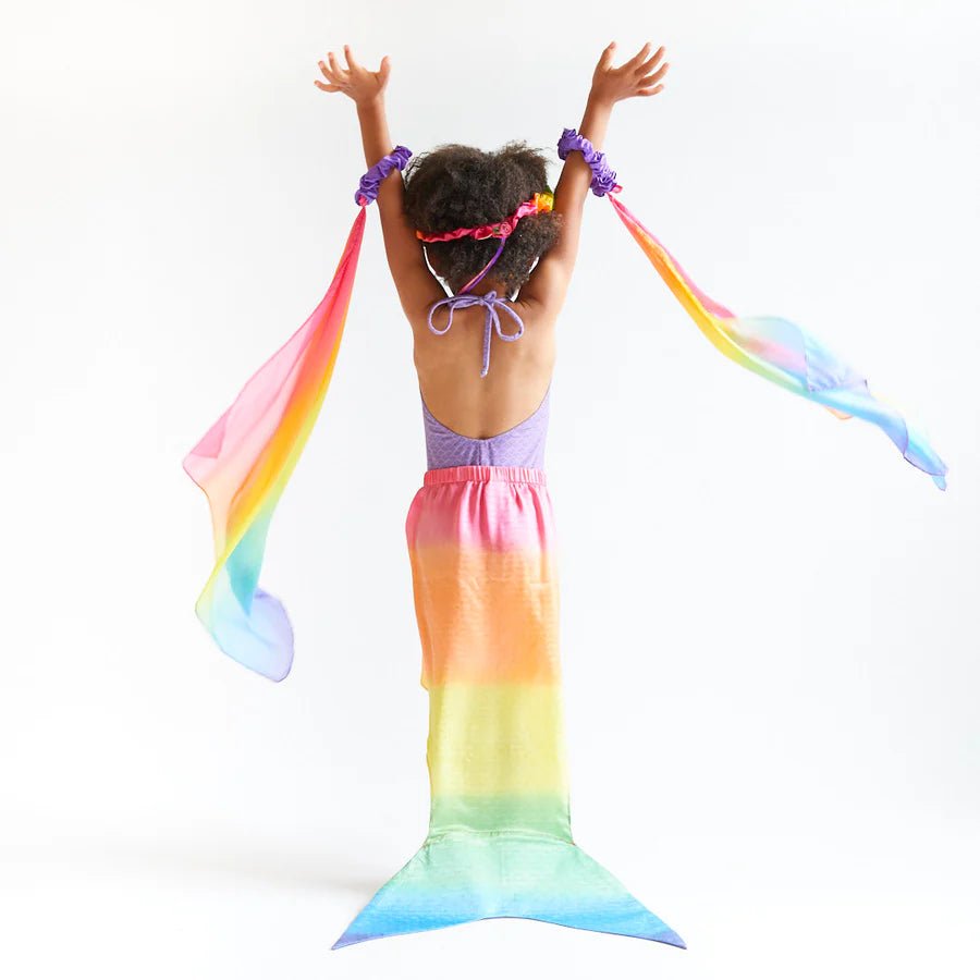 Child wearing a colorful mermaid tail with rainbow streamers on a white background