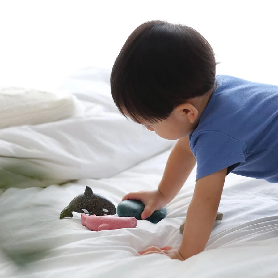 Child playing with wooden sea animal toys on a white bed
