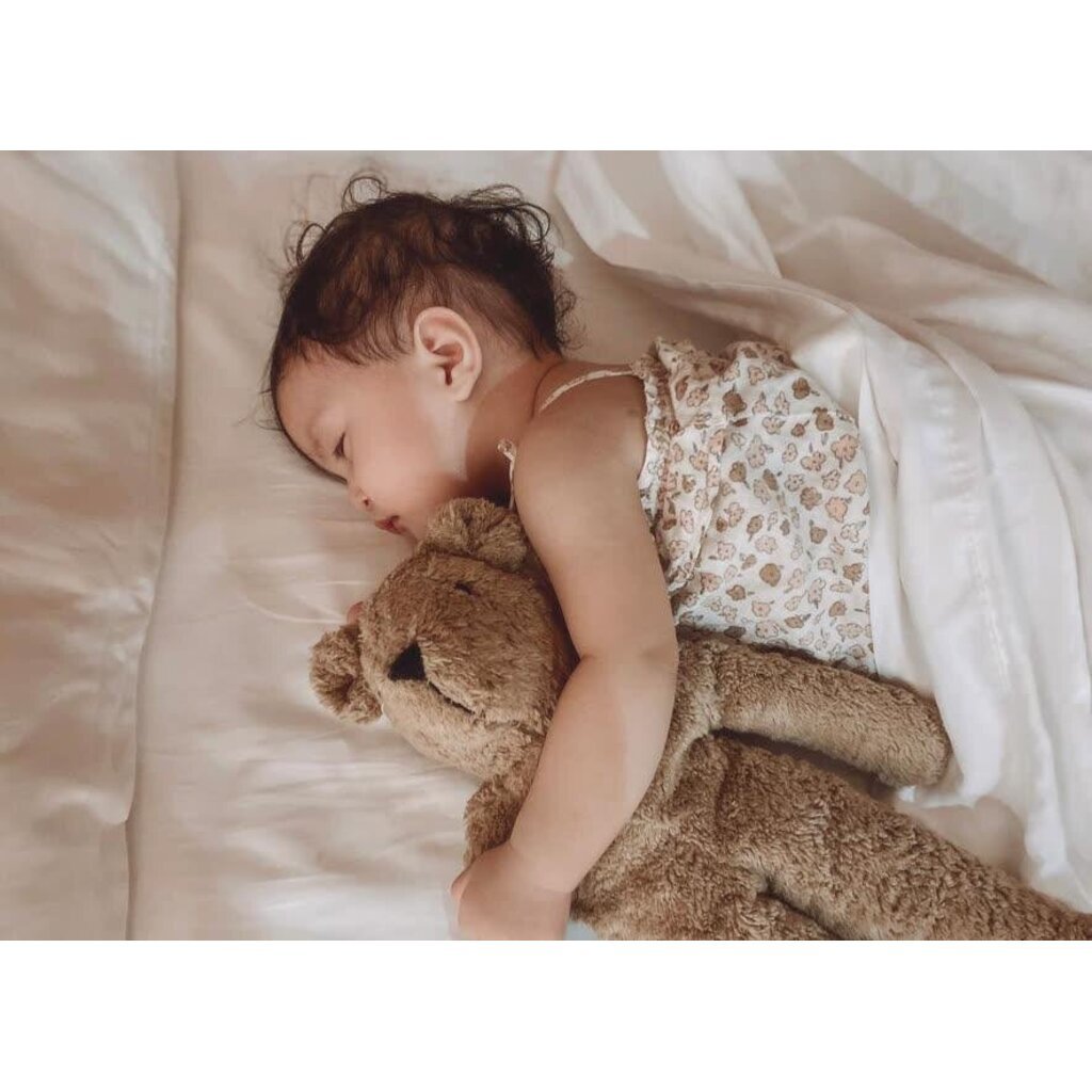 Child sleeping with a Senger beige teddy bear on a soft surface