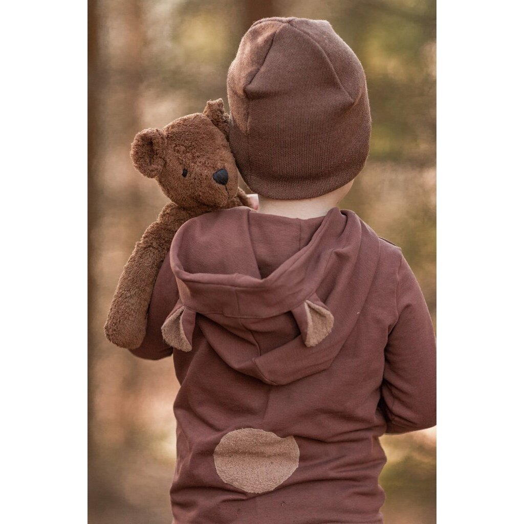 Child wearing a brown outfit with a hood and bear ears, holding a Brown Senger teddy bear.