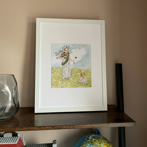 Framed illustration of a woman and child in a meadow on a shelf against a beige wall