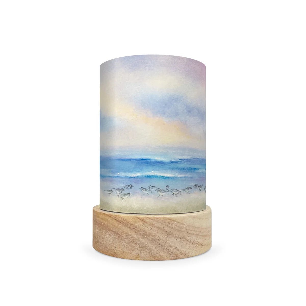 A cylindrical decorative lamp shade with a watercolor-style ocean scene printed on the shade, resting on a round natural wood base against a plain white background.