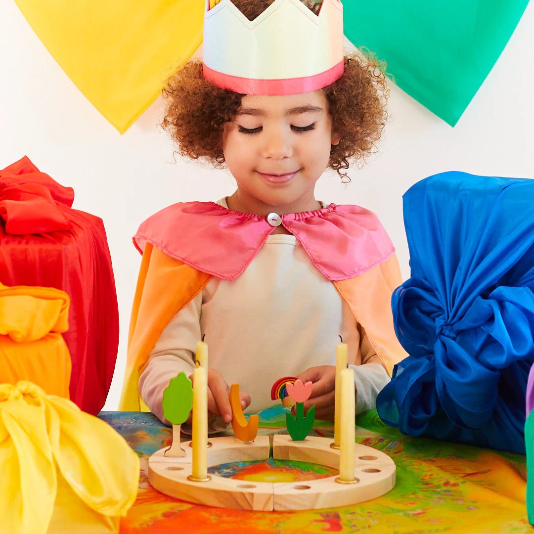 Child in colorful costume playing with wooden birthday ring, surrounded by colorful decorations