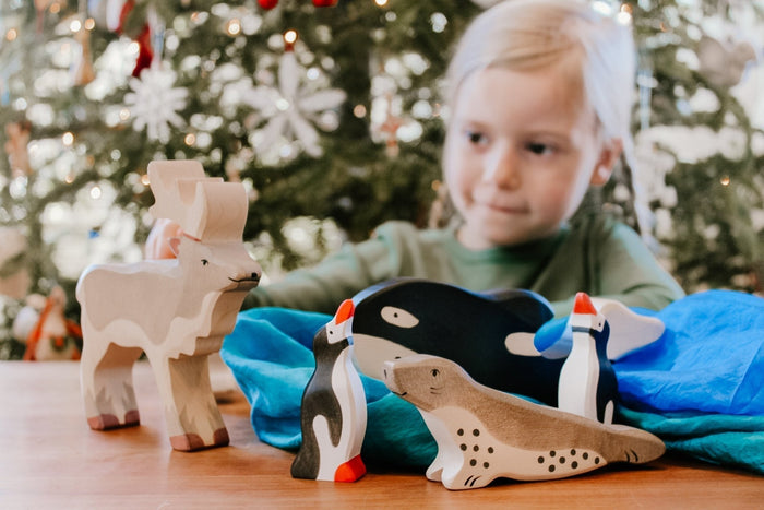 Favorite Christmas treasures. Little girl playing with wooden Christmas toys against the background of a Christmas tree.