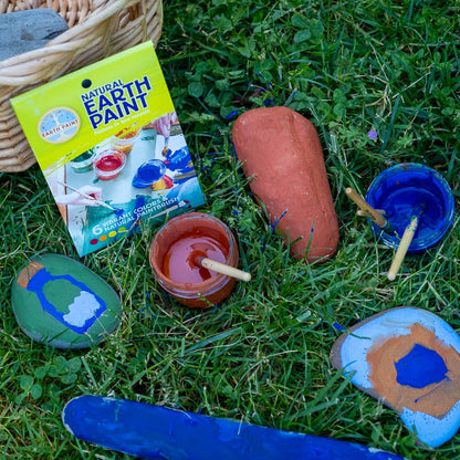 Cups of blue and red paint in the grass surrounded by painted rocks