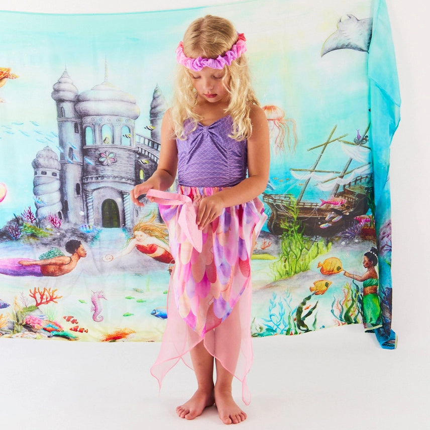 Child wearing a pink mermaid skirt and matching headband against an underwater themed playsilk