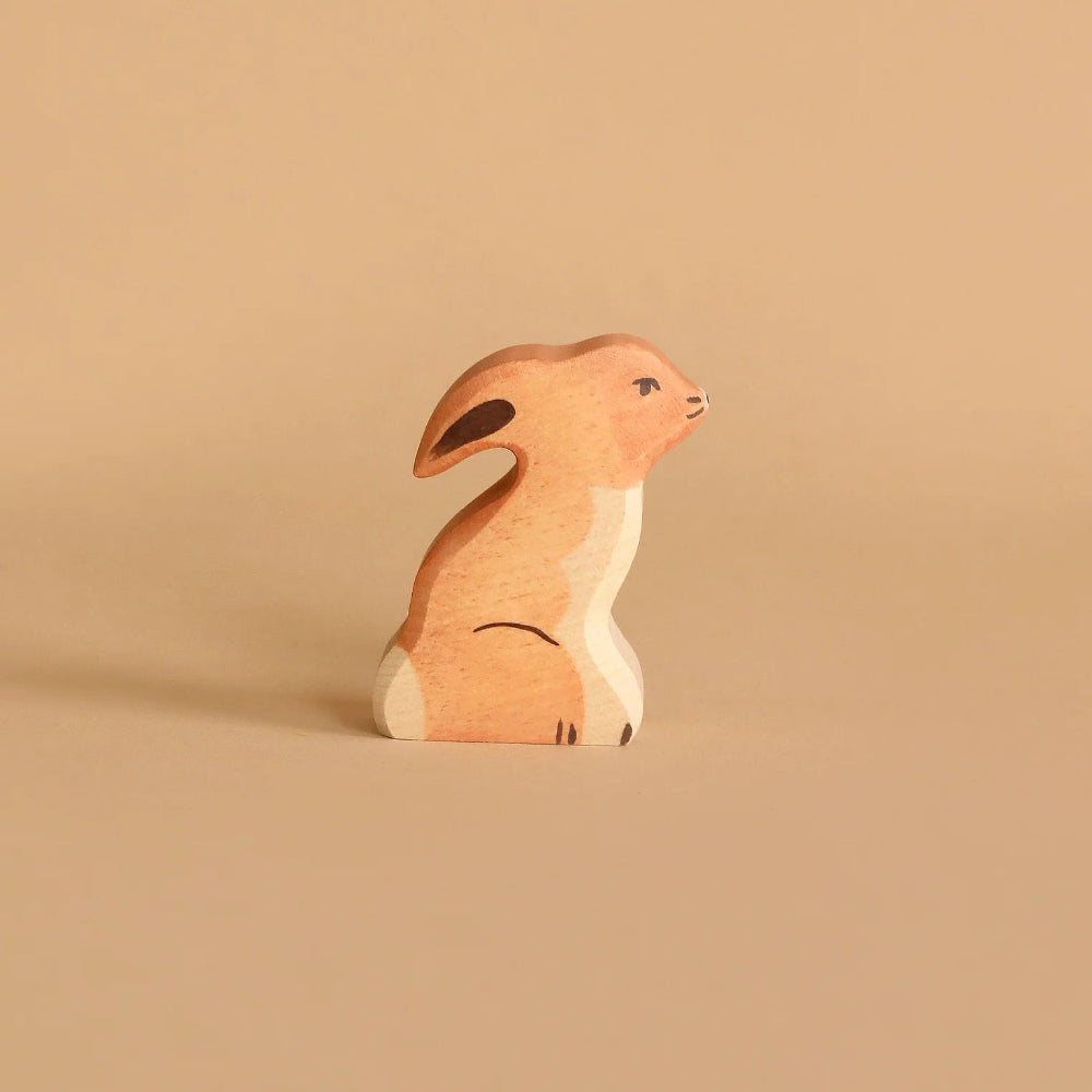 Wooden tan rabbit sitting upright against a light colored background