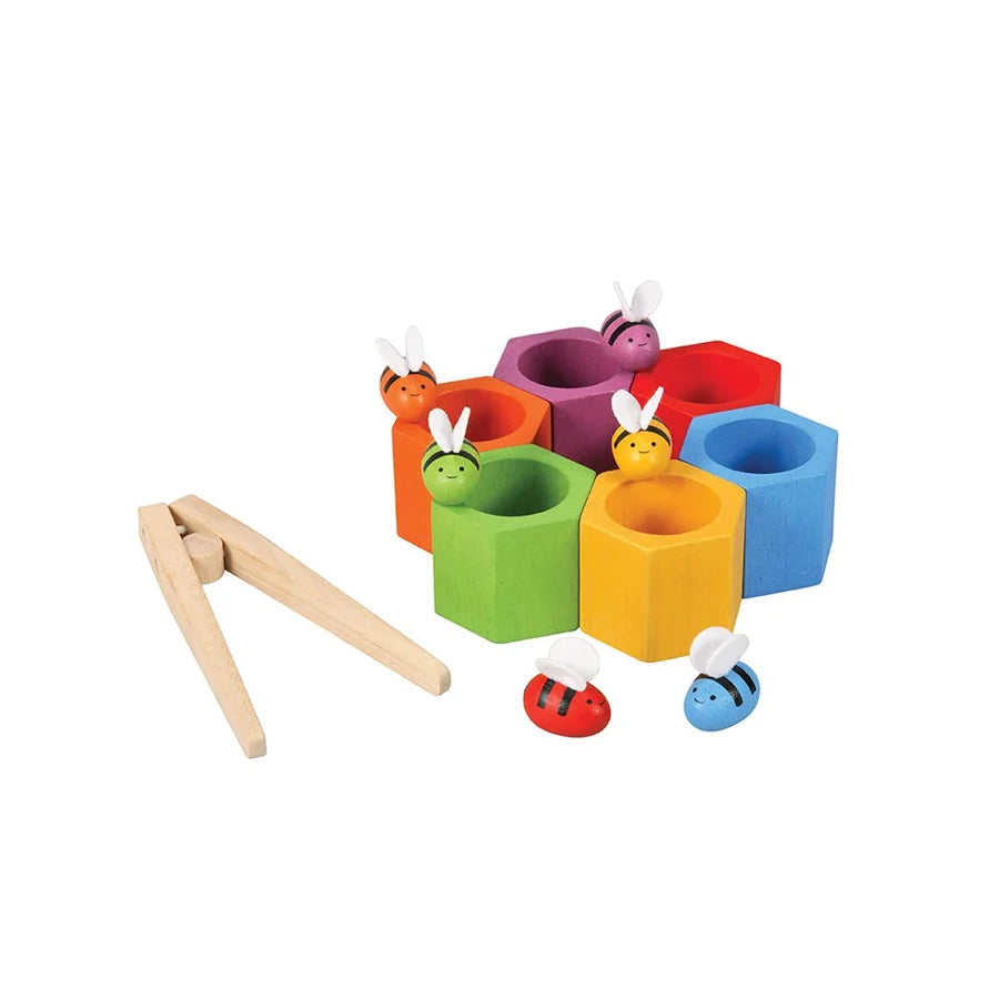 6 hexagonal wooden beehives arranged in a circle with wooden tongs and wooden bees on a white background
