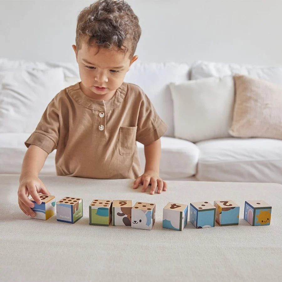 Child standing in front of wooden number blocks laid out on a table with a white couch in the background
