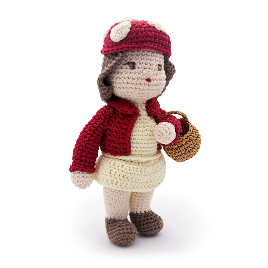 Side view of crocheted doll with red sweater and mushroom hat, holding a brown basket against a white background
