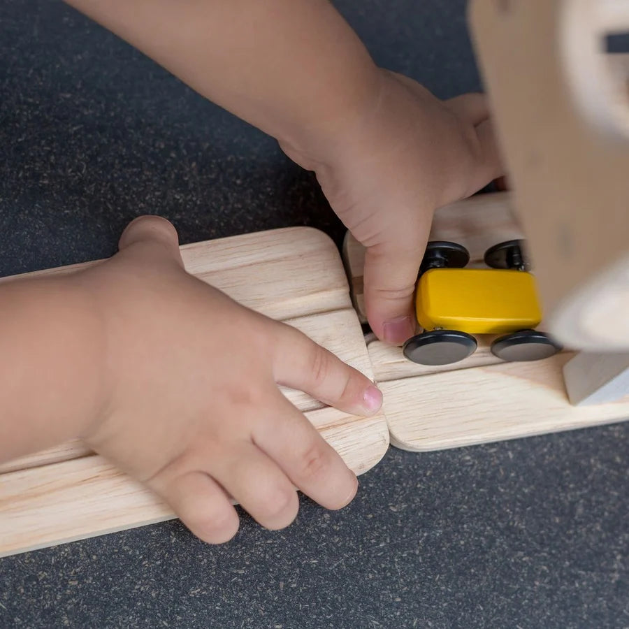 Two small hands putting together two pieces of race track with a yellow wooden car off to the side