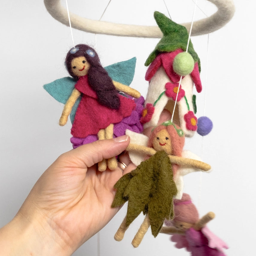 Hand holding two needle felted fairies suspended from a mobile against a white background
