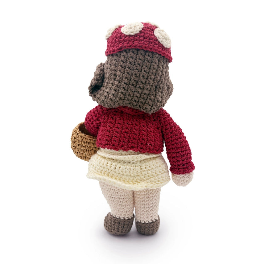 Rear view of a crocheted doll with a red sweater and cap holding a brown basket against a white background