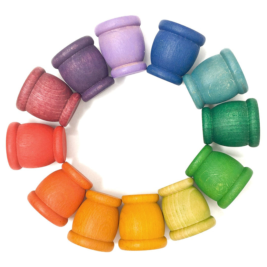 12 wooden cups in 12 rainbow colors arranged in a circle on a white background