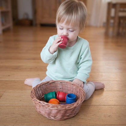 Small child playing with a basket of colorful wooden cups on a wooden surface