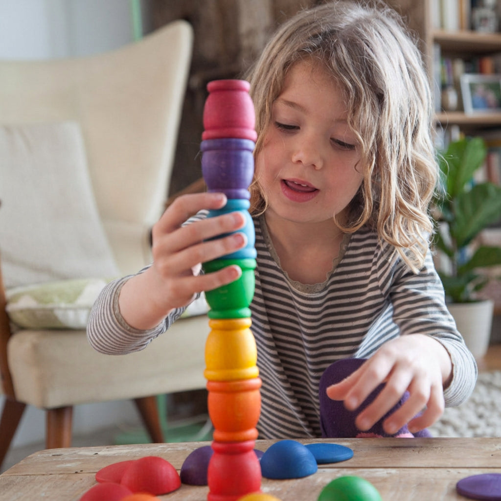 Young child stacking wooden cups on a wooden surface in a living room setting