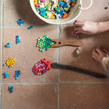 Top down view of child's hands playing with small wooden pieces sorted by color on a tile floor
