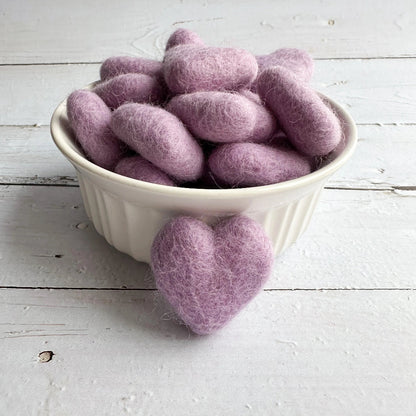 White bowl filled with light purple felted hearts on a light wooden surface