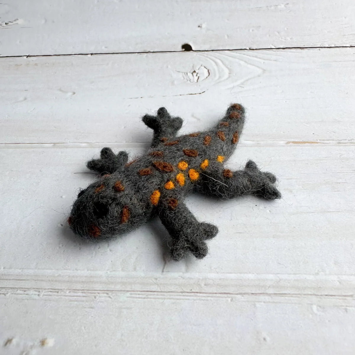 Gray felted salamander with orange spots on a light wooden surface