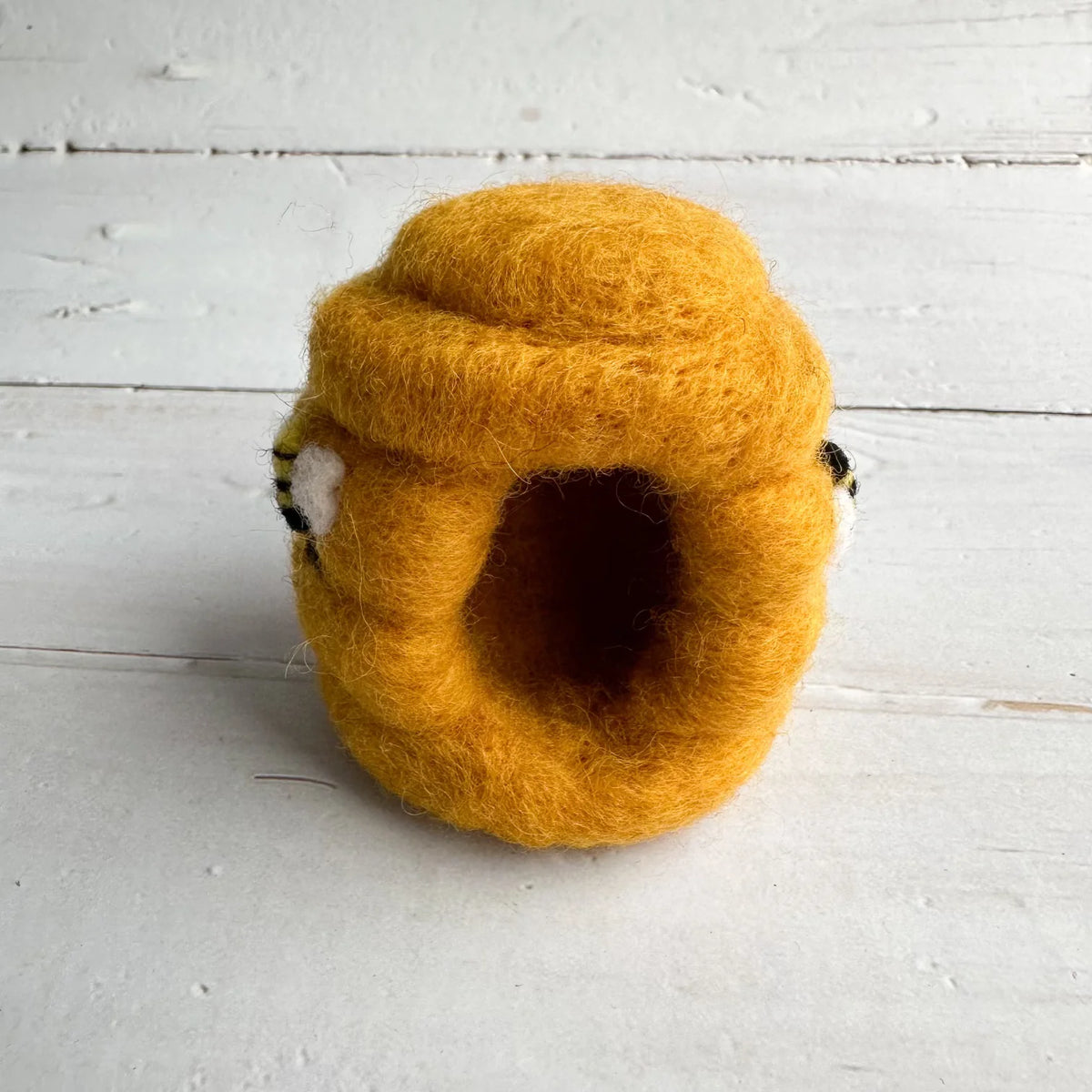 Yellow felted wool beehive house on a white wooden surface