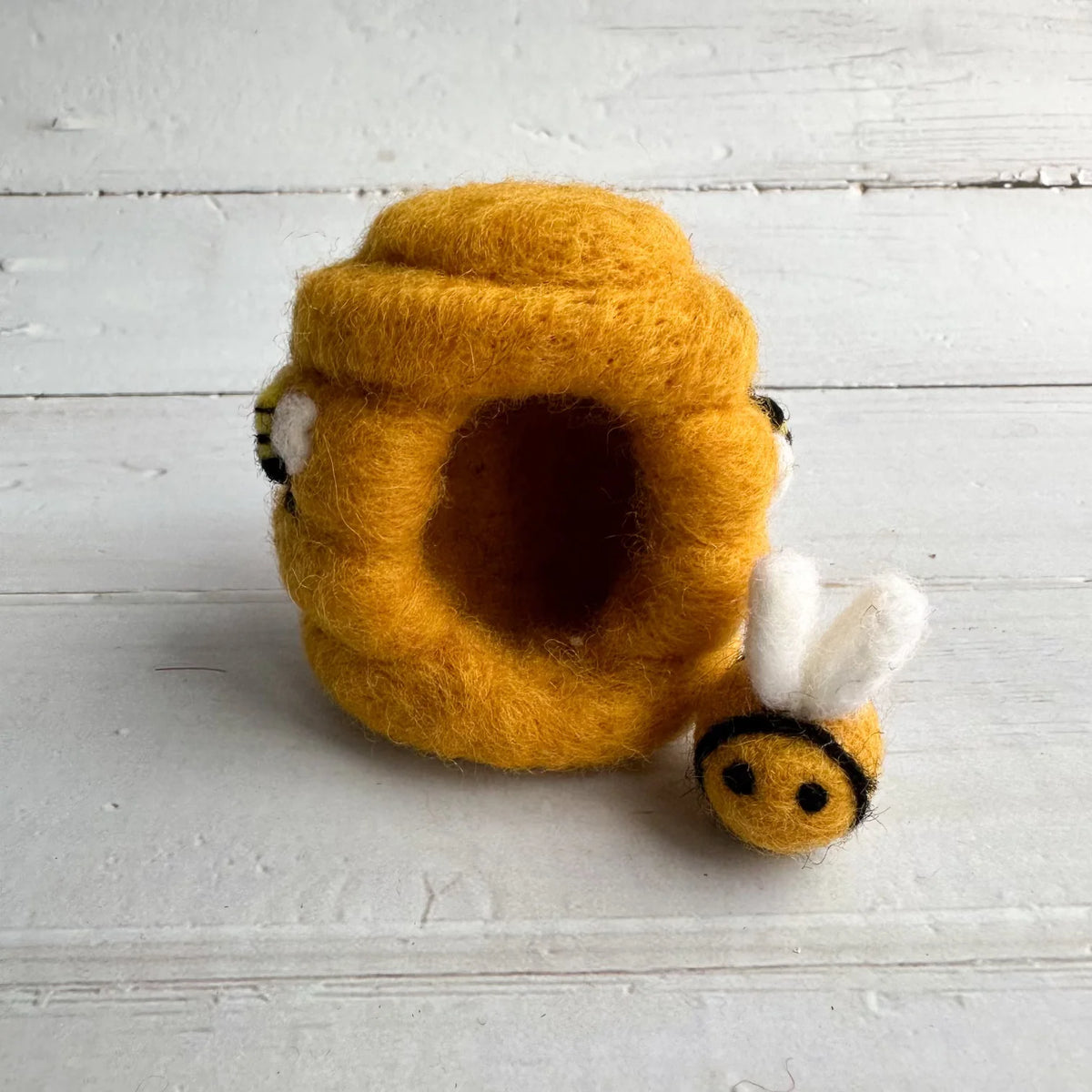 Yellow felt bee hive with a bee on a light wooden surface