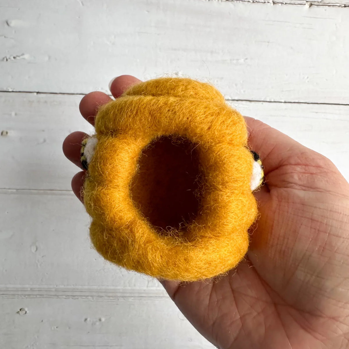 Hand holding a yellow felted wool beehive against a white wooden background