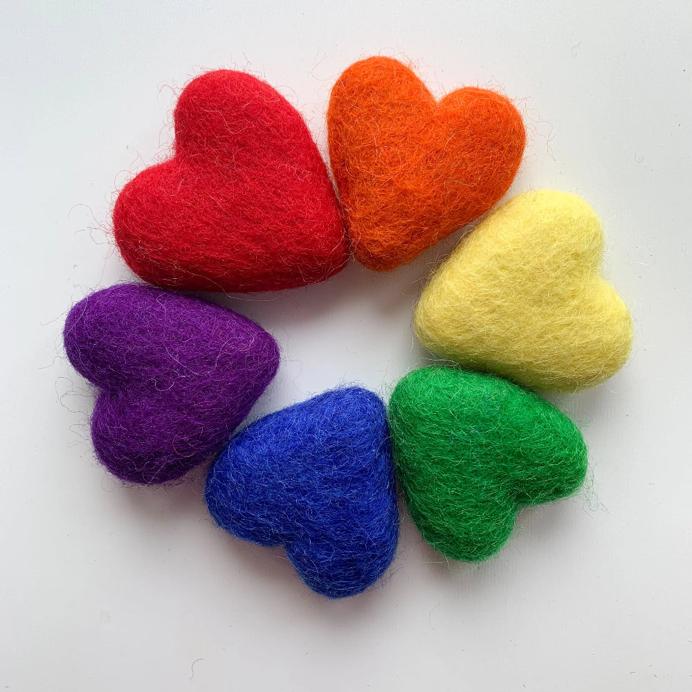Six felted wool hearts in red, orange, yellow, green, blue, and purple arranged in a circular pattern on a plain white background.