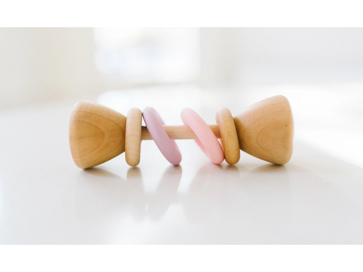 Wooden baby rattle with pink and purple accents on a white background