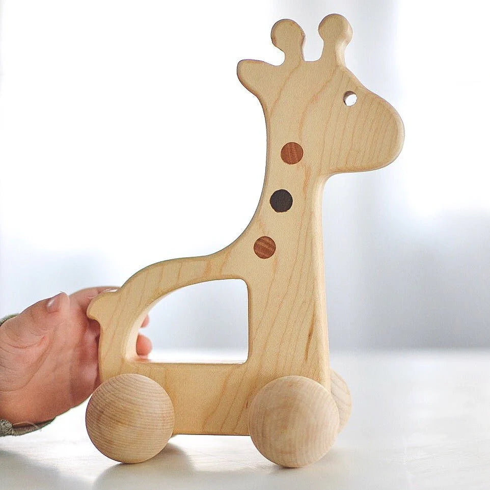 Wooden giraffe toy with wheels held by a hand on a light background