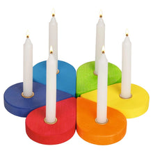 A six-piece wooden candle holder set featuring six colorful bases in red, orange, yellow, green, blue, and purple, each holding a white candle. The candles are lit, and the items are photographed on a clean white background.