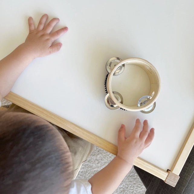 Child playing with a small tambourine on a white surface