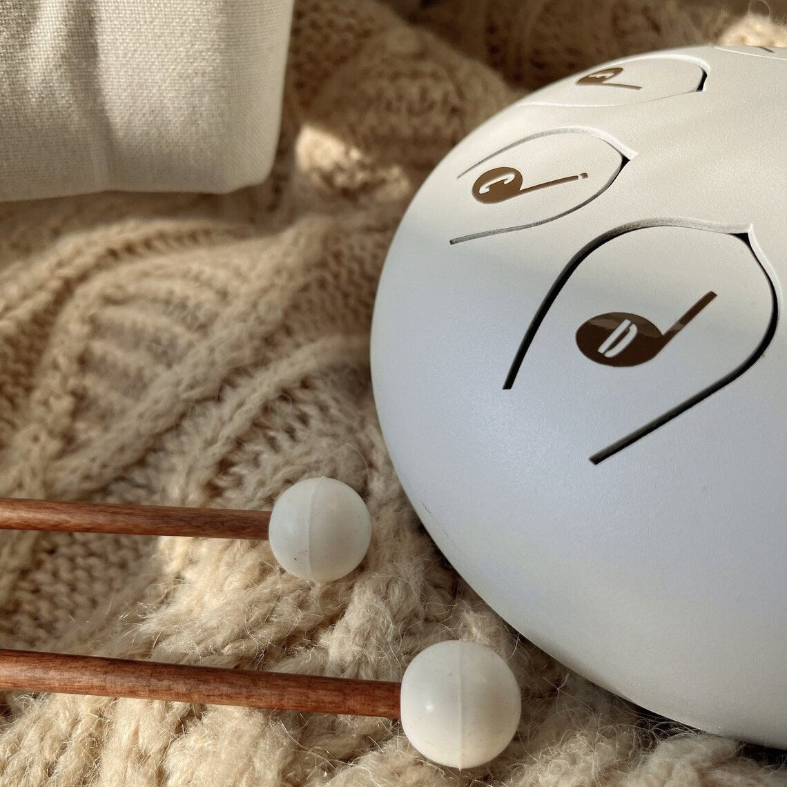 White steel drum and two drum sticks on a beige knitted surface