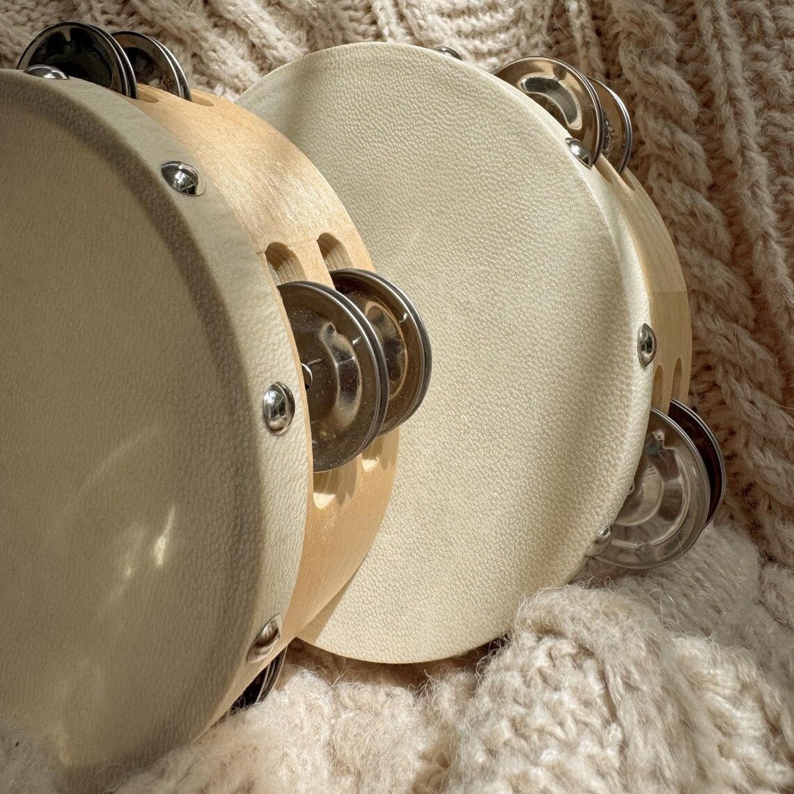 Close-up of two beige tambourines on a textured beige fabric background