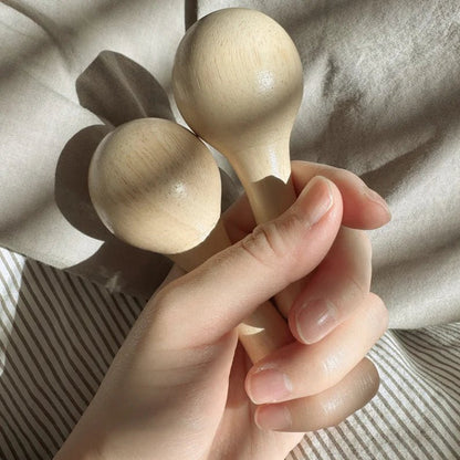 Hand holding two wooden rattles against a neutral background