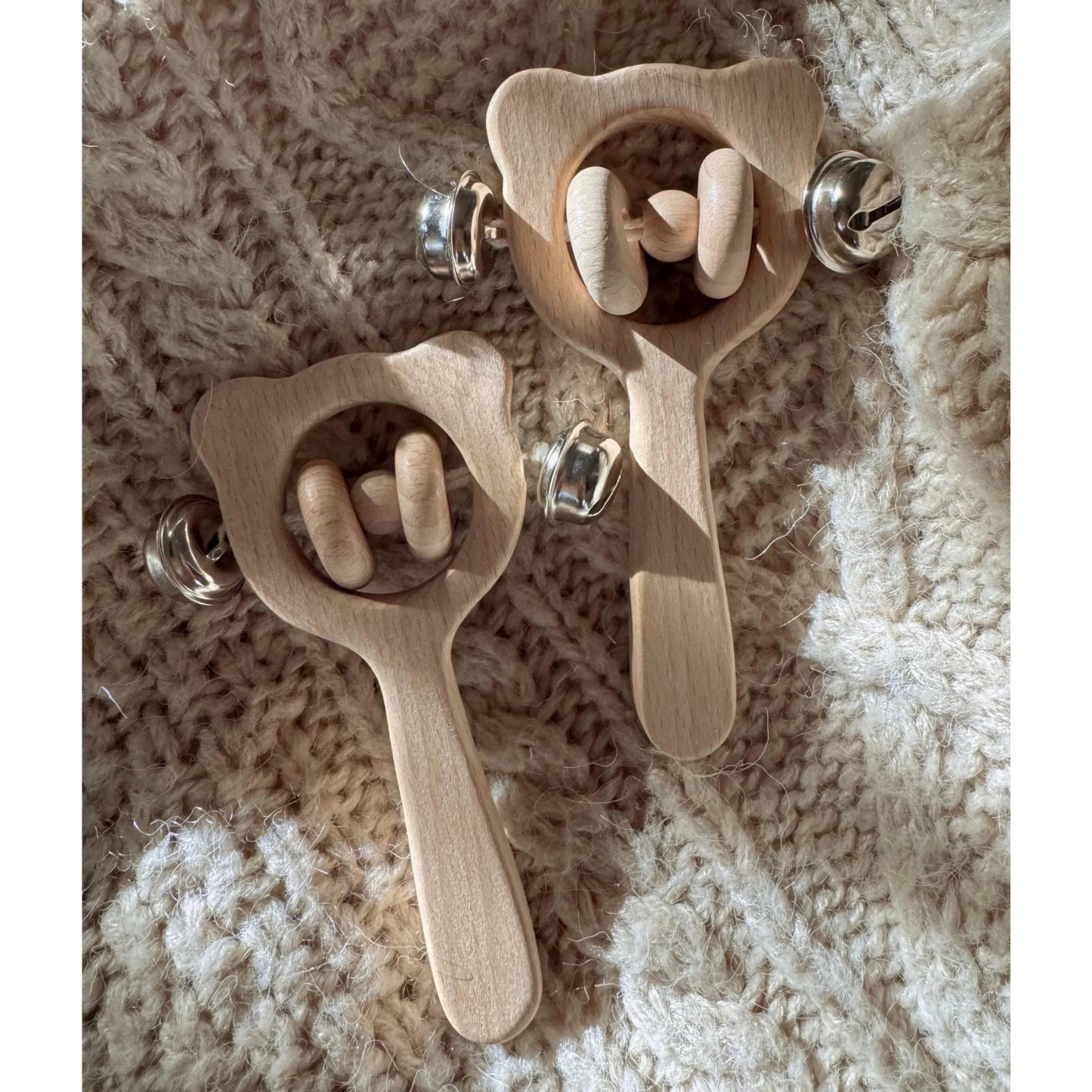 Two wooden baby rattle toys on a textured beige surface