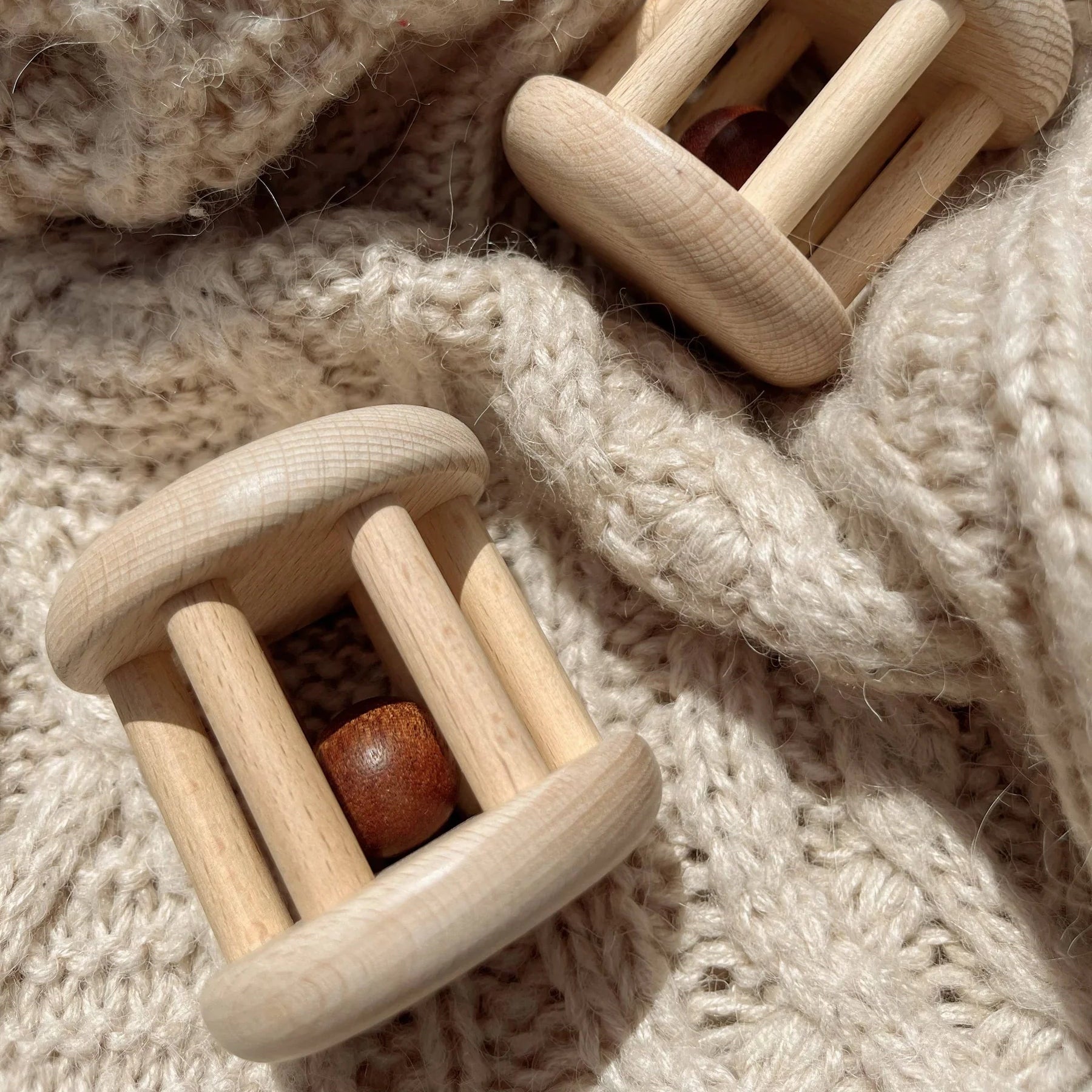 Two wooden baby rattles on a soft, textured fabric background